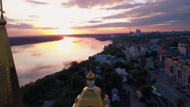 Aerial view of the sunset sky above the wide river. Clip. Green town located along the river.