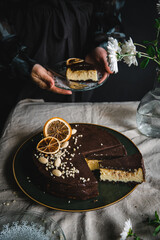 Ukrainian cheesecake syrnyk with chocolate and almond glaze cut on pieces with woman holding a piece on plate on background.
