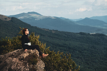 Młoda dziewczyna odpoczywa w górach w czasie wakacji siedząc na skale na szlaku prowadzącym na Połoninę Wetlińską, Bieszczady, Polska - obrazy, fototapety, plakaty