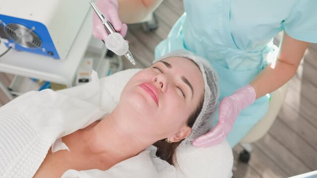Woman Beautician Makes Rejuvenating Facial Skin Procedure of a Female Client. Professional Cosmetic Procedures in Modern Beauty Clinic and Spa Services. Concept Skincare and Cosmetology. Slow Motion.