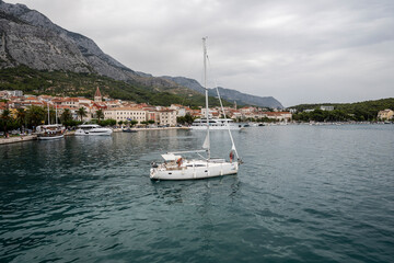 Sailboat leaving port of Makarska, popular tourist town on croatian coast, under mighty Biokovo mountain