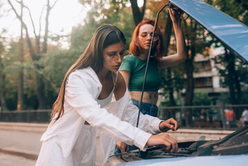 Two women with broken car on the road. Open hood