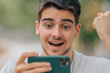 excited young man playing or looking at mobile phone