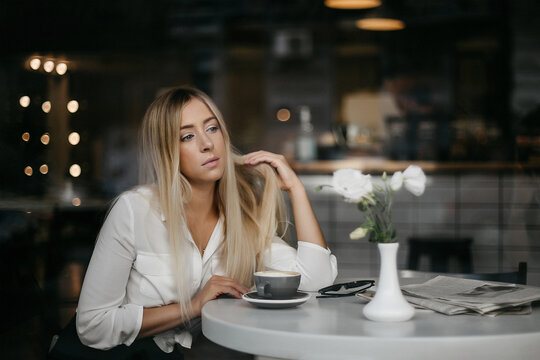 Front View Of Woman Having Coffee Break While Resting In The Cafe. Serious Woman, With Blond Hair, Wearing Formal Apparel, Enjoying Of City View And Drinking Ordered Coffee