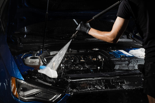 Pouring water on car engine. Washing car engine with spray, brush and detergent in detailing auto service. Detailing cleaning motor from dust and dirt.