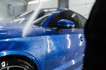Car washer pouring water for full body car wash. Spraying water on car to wash off foam in the...