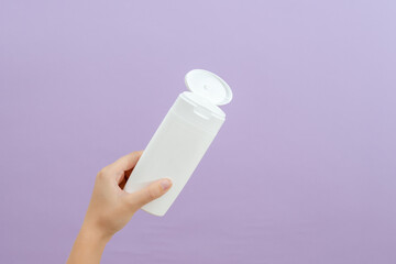 Cosmetic packaging tube in womans hand on lilac background. Beauty concept. Tube for cosmetic products