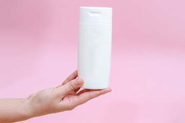 Woman holds a white bottle (cream, lotion, gel, shampoo) for cosmetic products isolated on pink background