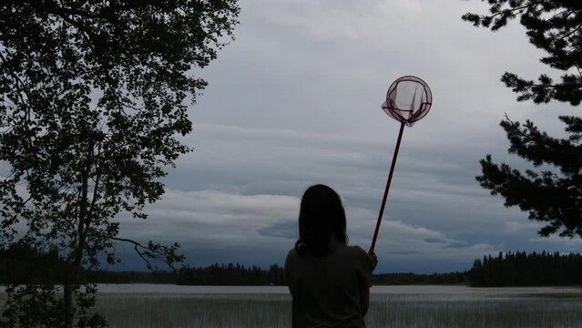Kid slowly waving a collection bag or net. Dark silhouettes. Cloudy sky in the background. Jämtland, Sweden, Europe.