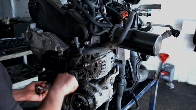 Professional auto mechanic unscrewing a crankshaft pulley bolt with a socket wrench during engine disassembly and repair in a specialized automotive service garage