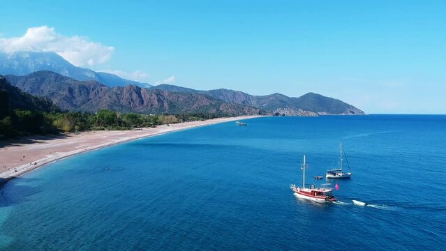 Two yachts warm up in the Mediterranean near ancient Olympus. The photo shows Takhtala mountains and the blue sea and a sandy beach.