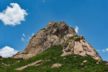 mountain that looks like an elephant, covered with green trees on a cloudy blue sky