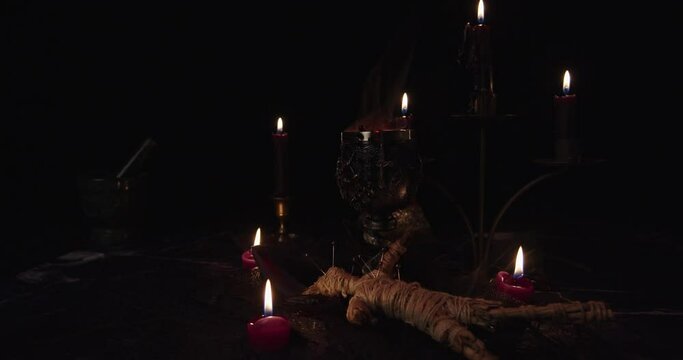 Still Life Satanic with steaming sacrificial cup and candles with black background.