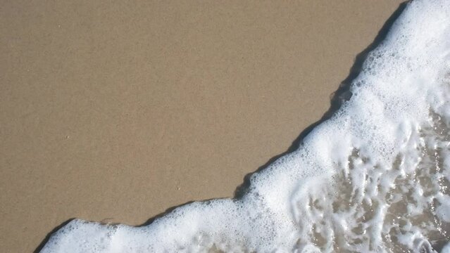 Top view slow motion Full HD video banner with sand, sea foam and waves. Scene of top view beach and seawater on sandy beach in summer. Nature and travel concept