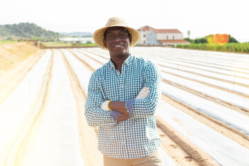 Smiling african american farmer standing against background of farm plantation covered with...