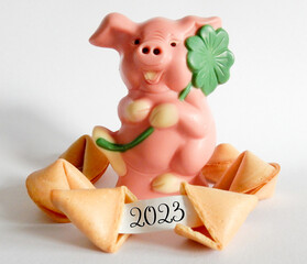 Rosa Schweinchen aus Schokolade mit Kleeblatt und Glückskekse, ein Glückskeks geöffnet mit Datum 2023 auf den Papierstreifen,
Silvester und Glücksbringer Karte,
