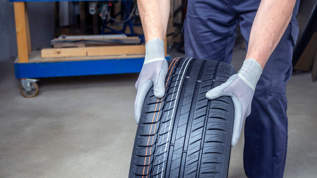 MECHANIC'S HANDS CARRYING TIRE IN WORKSHOP. TYRE PUNCTURE REPAIR. CAR MAINTENANCE FOR SAFETY. 
