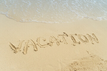 Word Vacation on beach - summer concept background. Sea, wave, sand, inscription vacation on the sand.