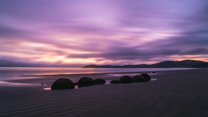 Panoramic shot of the calm sea with a sandy beach under the purple sky at sunset, New Zealand