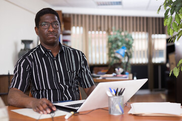 Concentrated african american businessman working with laptop and papers at office desk