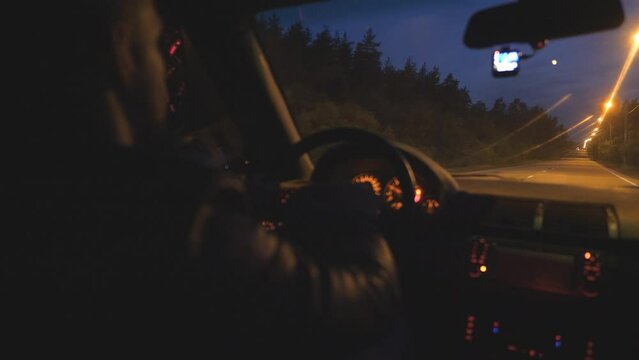 Male driver holds hands on steering wheel and rides in auto on highway at night time. Guy drives a modern automobile at evening. Young man moves in his SUV car on empty road. Close up Slow motion
