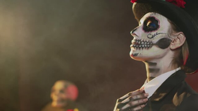 Female adult in halloween costume with skull body art celebrating holy mexican tradition, posing in studio. Looking like lady of death at santa muerte ritual celebration. Handheld shot.