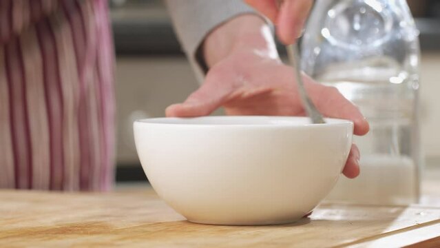 Woman Making Tahini At Home, Adding Water And Mixing In A White Bowl. Closeup Shot.