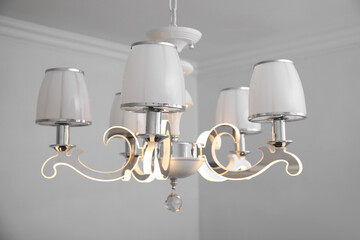 Stylish chandelier on ceiling in light room