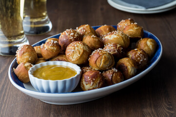 A platter of homemade pretzel bites with mustard dip and beer in behind. - obrazy, fototapety, plakaty