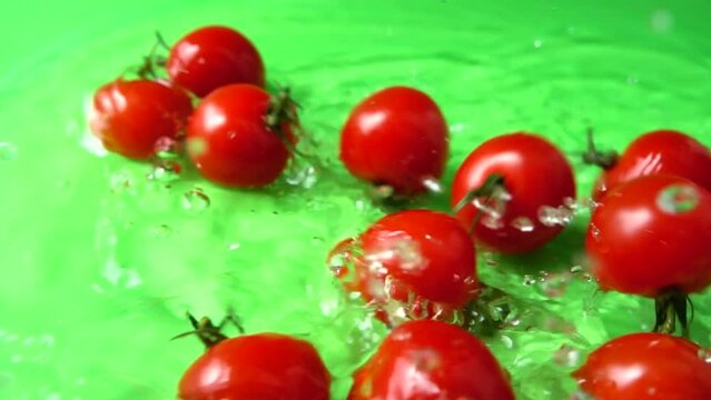 The falling cherry tomatoes in water. Slow motion.