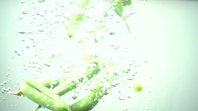 Falling of green peas in water. Slow motion.