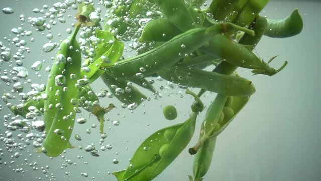 Falling of green peas in water. Slow motion.