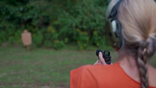 Closeup of mature, elderly woman fires a handgun at a shooting range target outside on a summer day.