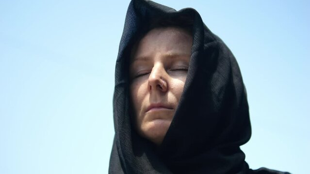 A close-up of the face of a widowed woman with a tired face and deep wrinkles from grief on it. She lost her man in the war. The widow closes her eyes and prays to God not to go crazy.
