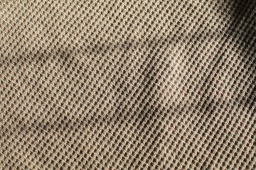 Beige waffle weave cotton fabric with light and shadow. Closeup of light natural cotton texture pattern for background.