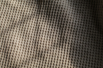 Beige waffle weave cotton fabric with light and shadow. Closeup of light natural cotton texture pattern for background.