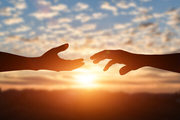 Silhouette of reaching, giving a helping hand, hope and support each other over sunset background. Help, friendship international day concept.