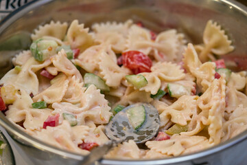 Pasta salad in a metal bowl with a spoon.