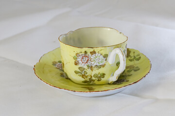 Antique Tea Cup and Saucer with a Floral Design on a White Tablecloth
