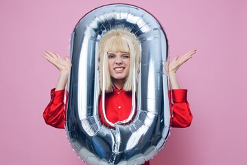 a funny, emotional woman stands on a pink background in a red shirt with an inflatable ball in the...