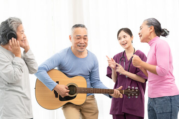 Group of senior people enjoying with activities together with doctor. Elderly people having fun concept. Happy senior playing guitar and singing songs having fun together.