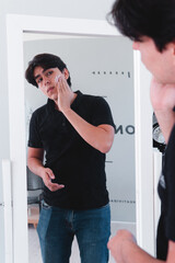 Fototapeta premium High quality photography. Caucasian boy in front of the mirror in his room applying face cream. Man taking care of his face with skin products.