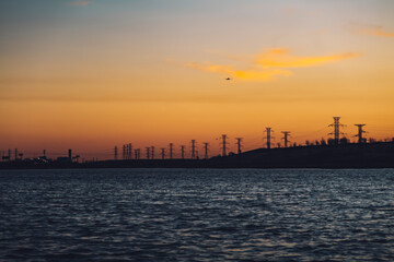 Obraz premium High voltage electricity tower sky sunset landscape, industrial background with water lake on front. High-quality photo
