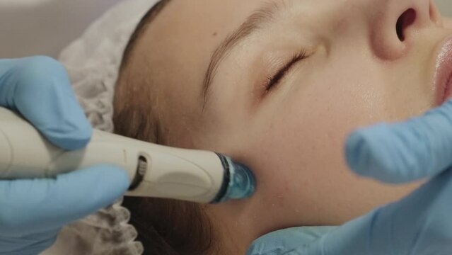 Young woman is relaxing getting vaccum facial hydro peeling procedure in beauty salon. Hardware face pores cleansing, close-up.