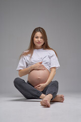 Young beautiful pregnant girl on a white background. A young mother smiles beautifully and enjoys pregnancy. Studio photo.