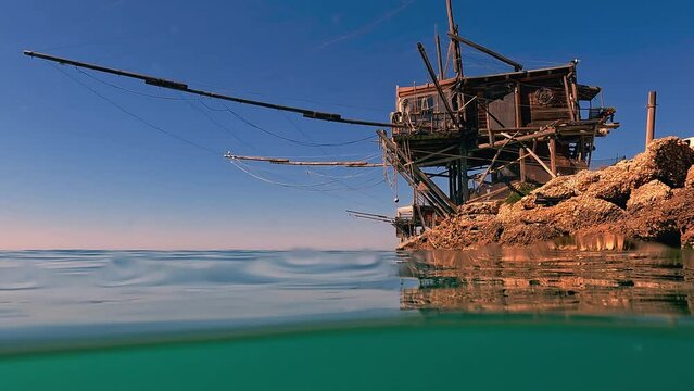 Split underwater view of trabocco or trabucco at Punta Penna beach in Costa dei Trabocchi  at sunset, Abruzzo in Italy. Low angle slow motion water surface edge view