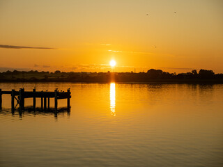 Fototapeta na wymiar Sunrise reflecting off lake with birds gathered on pier