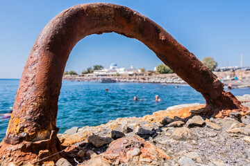 Rusty metal hook on the pier with the beach in the background - obrazy, fototapety, plakaty