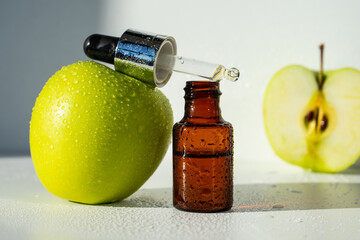 A bottle of apple essential oil and an eyedropper on a white table. Apple butter. Essential oil is...