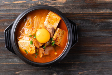 Korean food, Kimchi soup with tofu, pork and fresh egg yolk in Korean stone pot, Table top view
